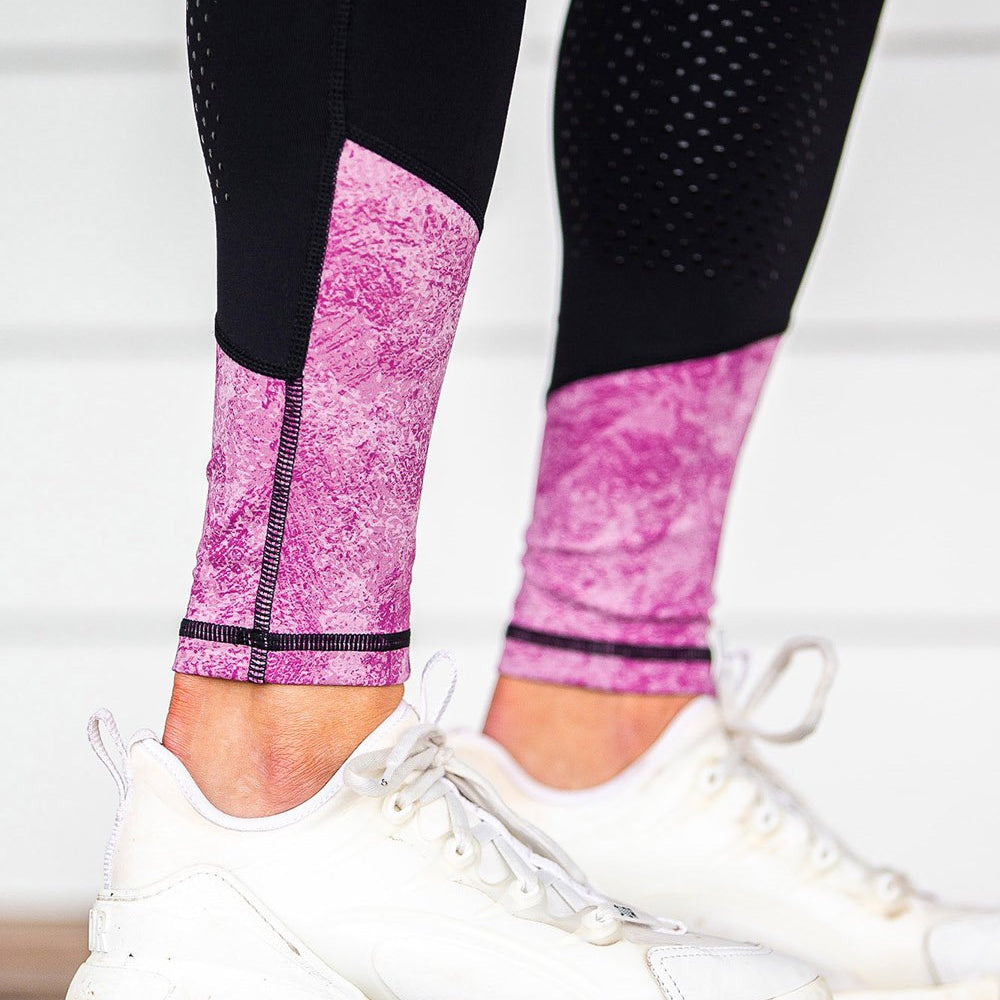Person wearing black and pink horse riding tights with white sneakers.