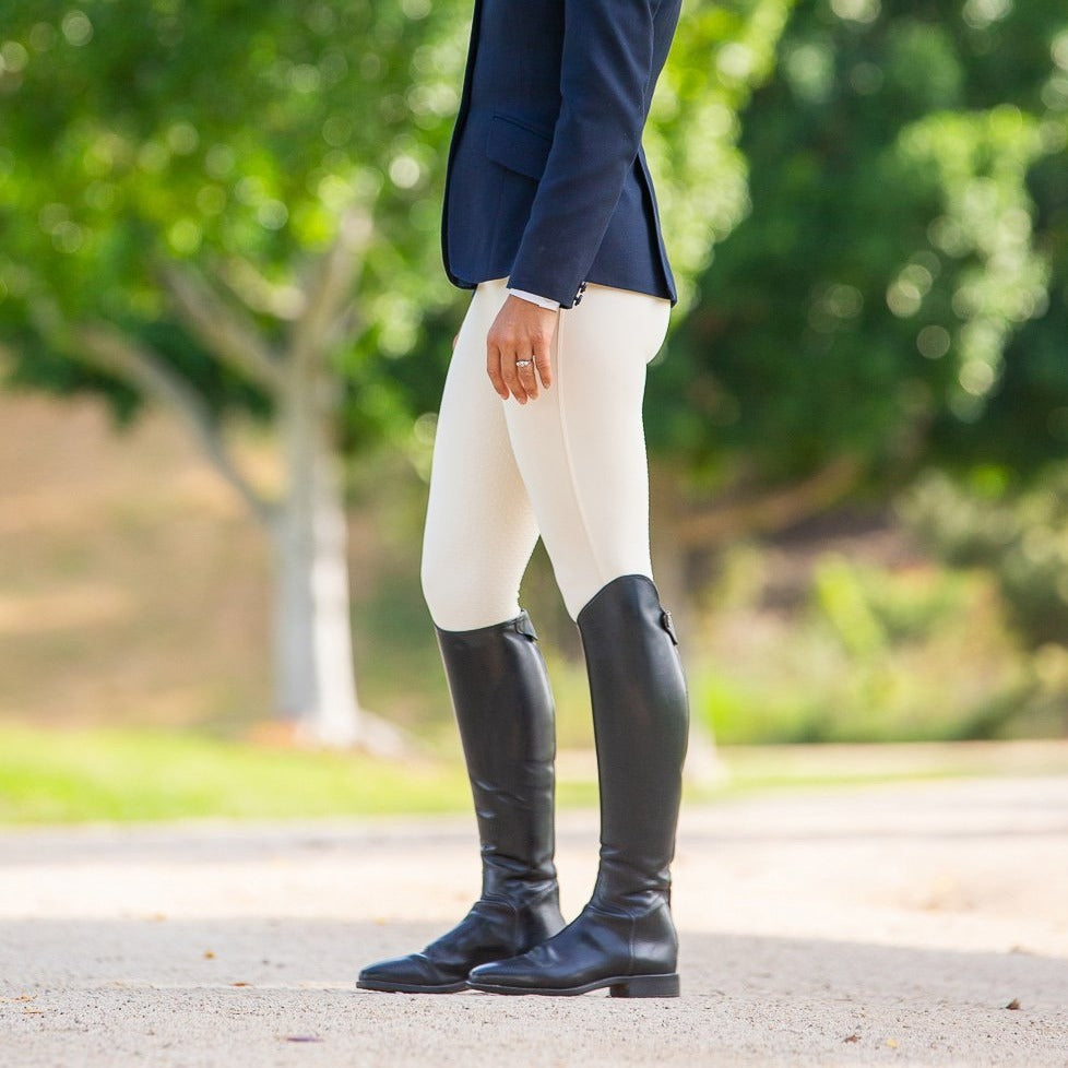 Person standing in horse riding tights and tall black boots.