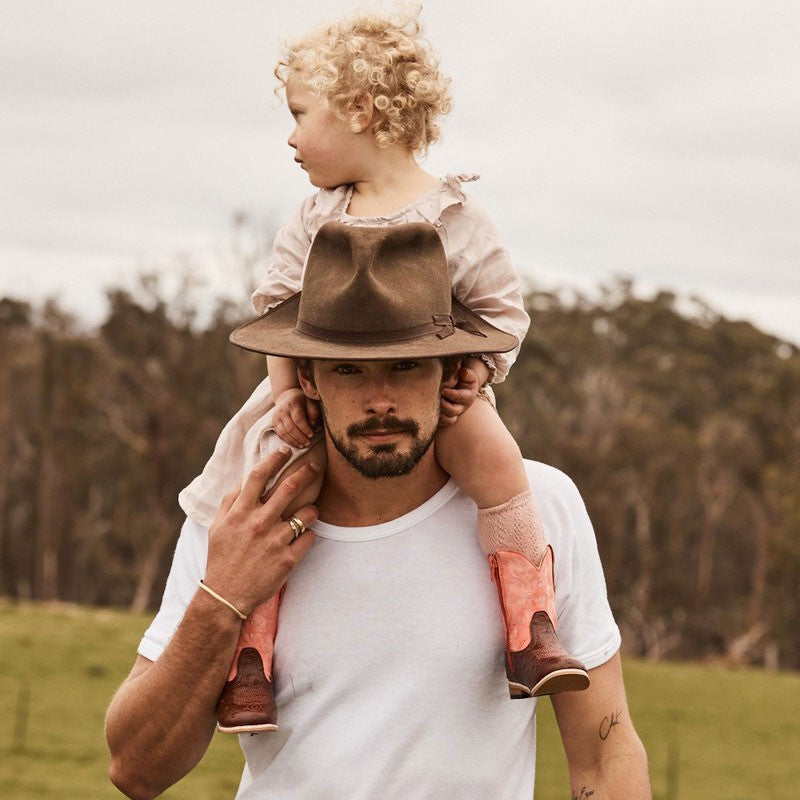 Man carrying child on shoulders, both wearing Baxter Boots.