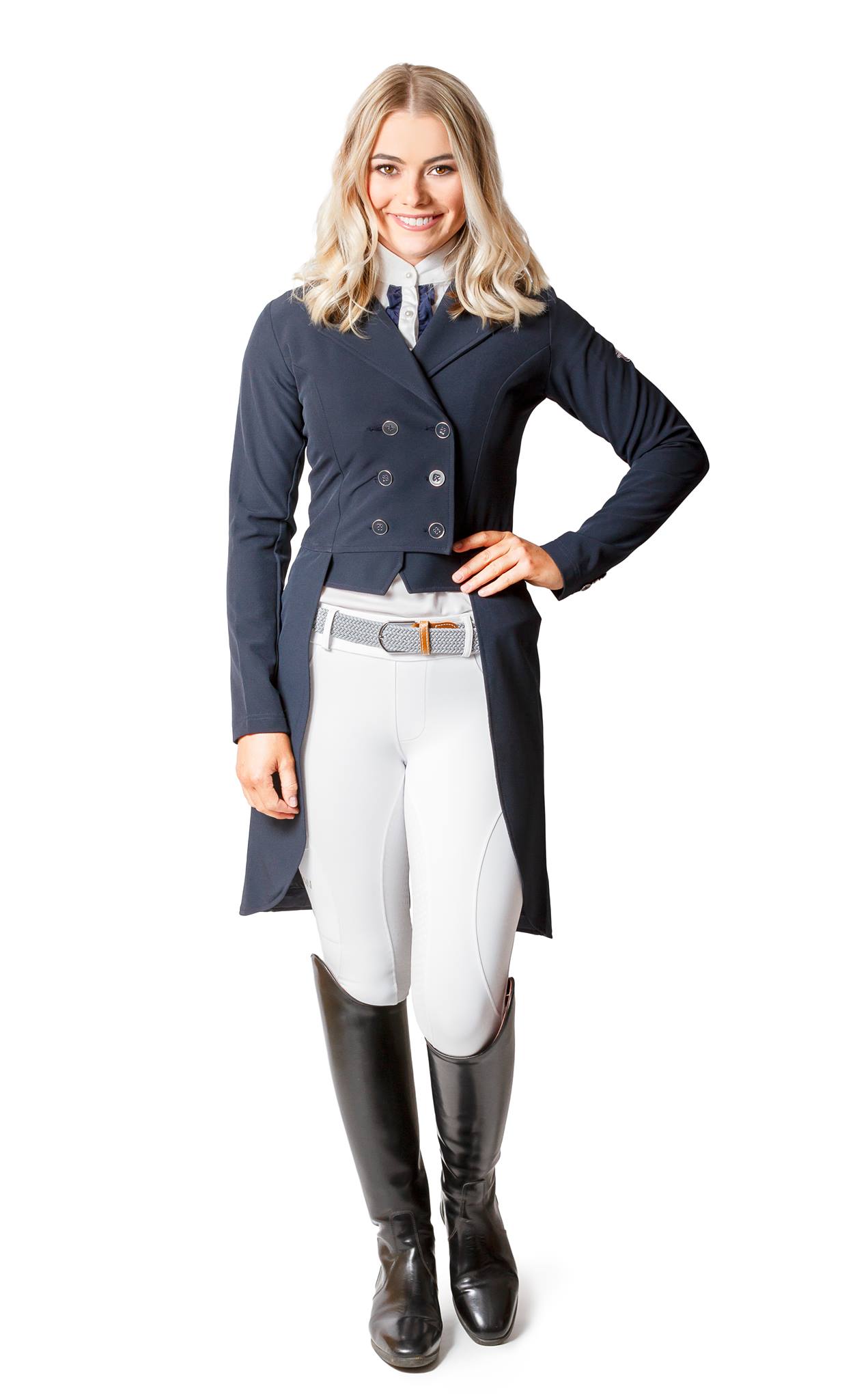 Woman standing in horse riding tights, navy jacket, and black boots.
