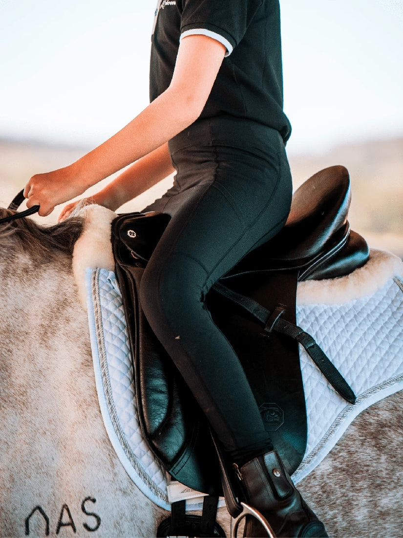 Person wearing black horse riding tights seated on a horse.