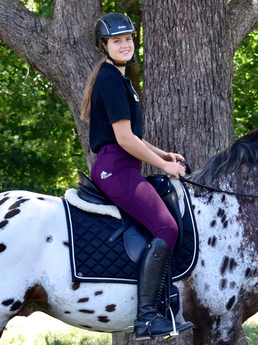 Smiling rider in helmet and purple horse riding tights on spotted horse.