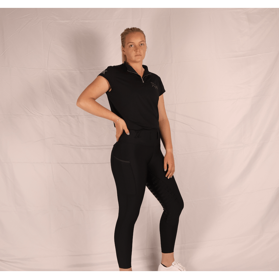 Woman posing confidently in black equestrian horse riding tights and shirt.