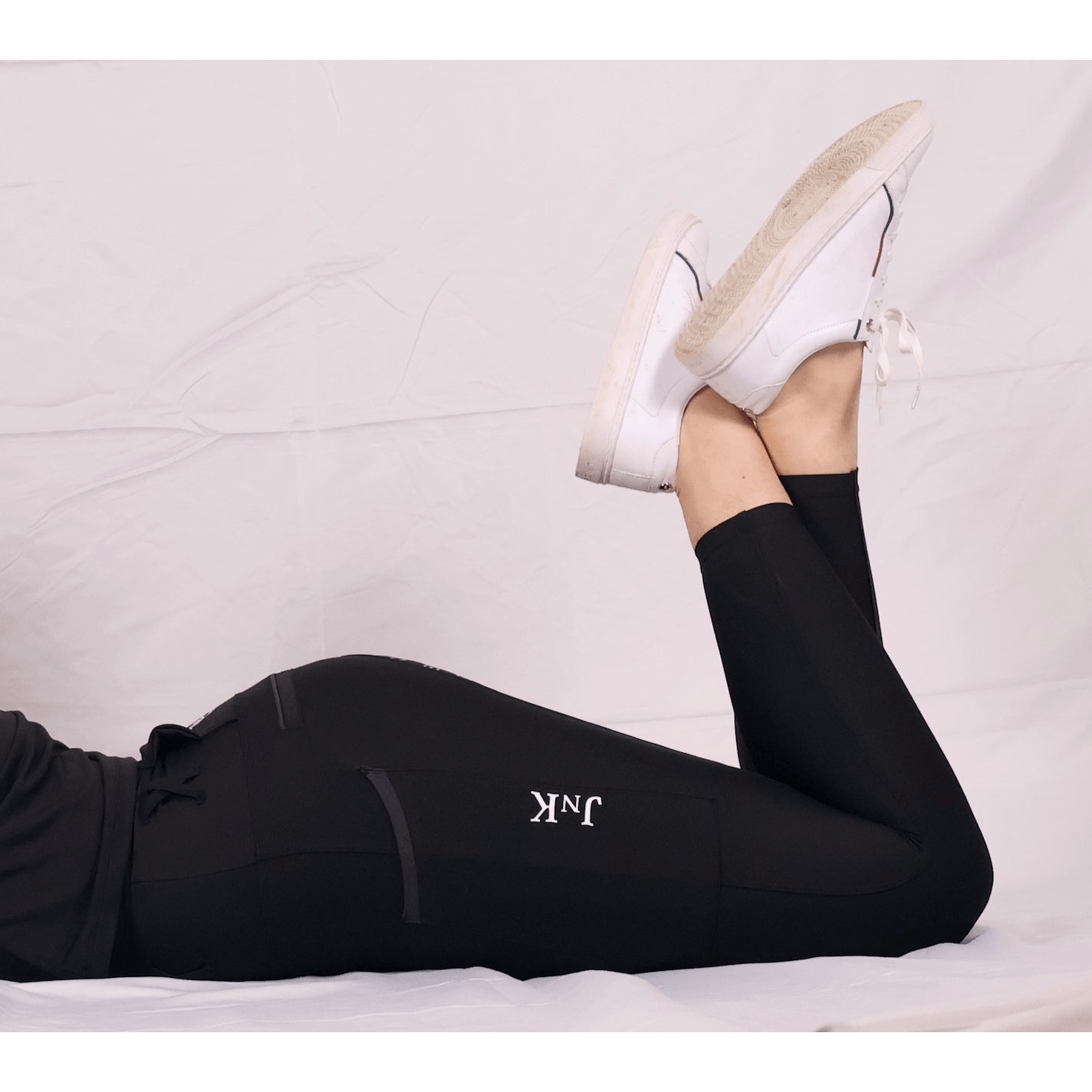 Person lying down showcasing black horse riding tights and white sneakers.