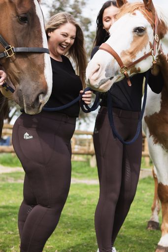 Two smiling women in horse riding tights holding horses' reins.