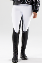 A person wearing white competition tights with a black seat, paired with a black jacket and black riding boots. The tights have silver logo detailing on the back pocket.