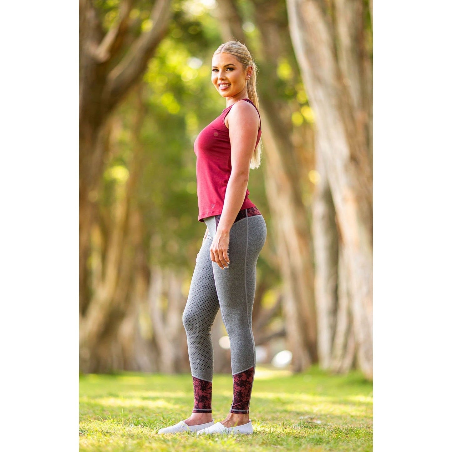 Woman in stylish horse riding tights stands smiling outdoors.