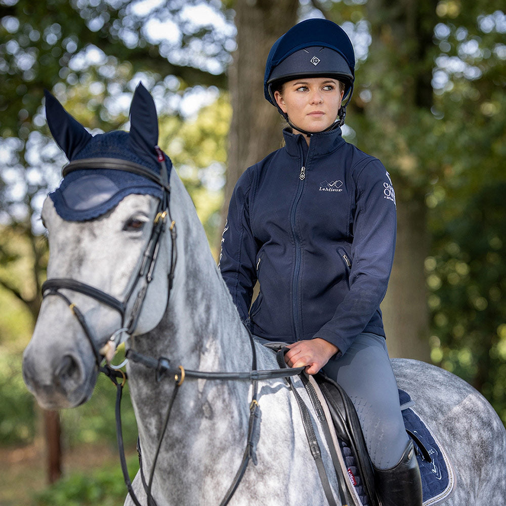 Rider in KEP equestrian helmet on grey horse, focused expression.