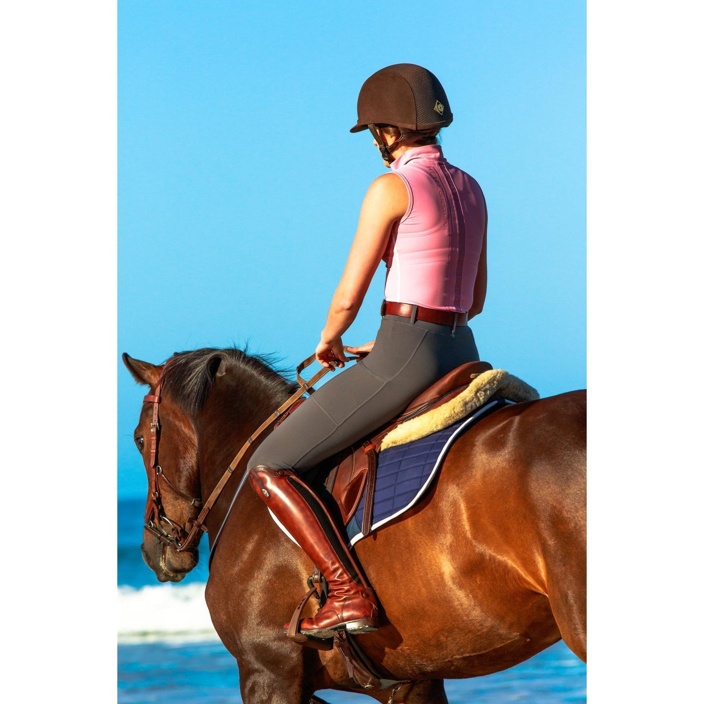Rider in helmet and horse riding tights on horseback by sea.