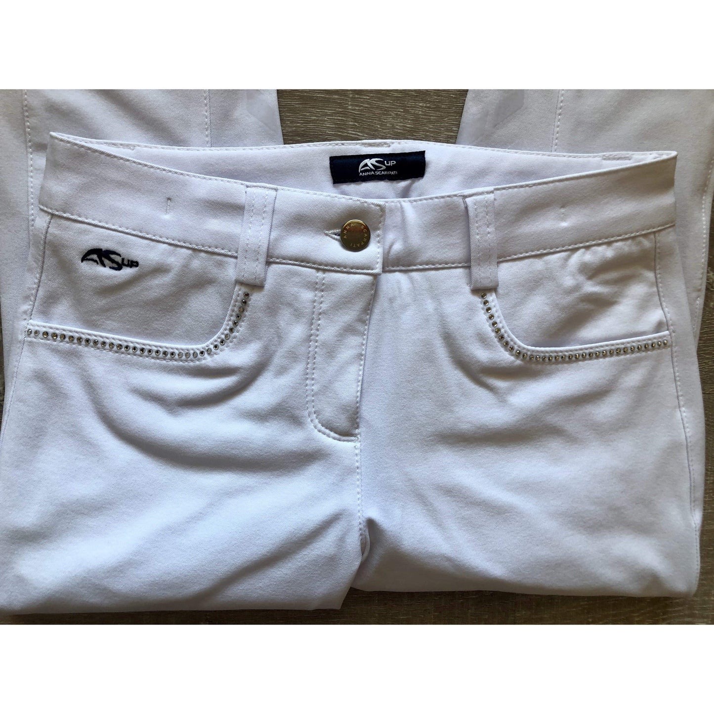 White Anna Scarpati pants with logo and rhinestone detail on pocket.