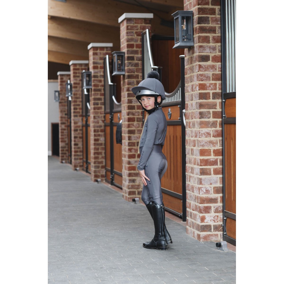 Young rider in helmet and horse riding tights by stable doors.