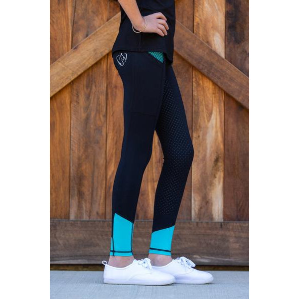 Woman wearing black horse riding tights with teal accents standing.