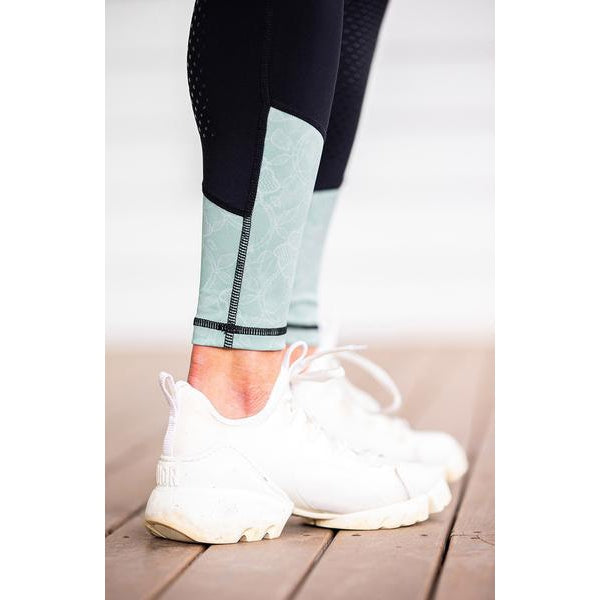 Person wearing black and mint green horse riding tights with white sneakers.