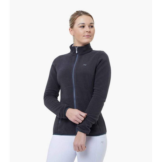 Woman in dark jacket and white horse riding tights standing.