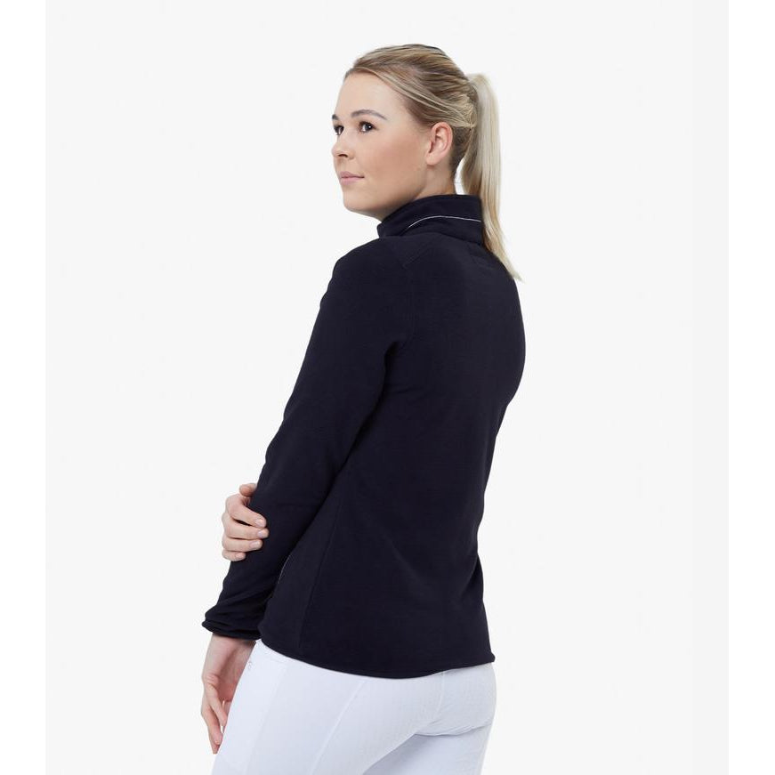 Woman in navy jacket and white horse riding tights, profile view.