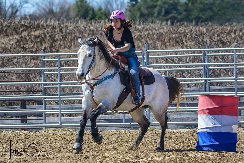 Rider on grey horse barrel racing at outdoor Thinline Global event.