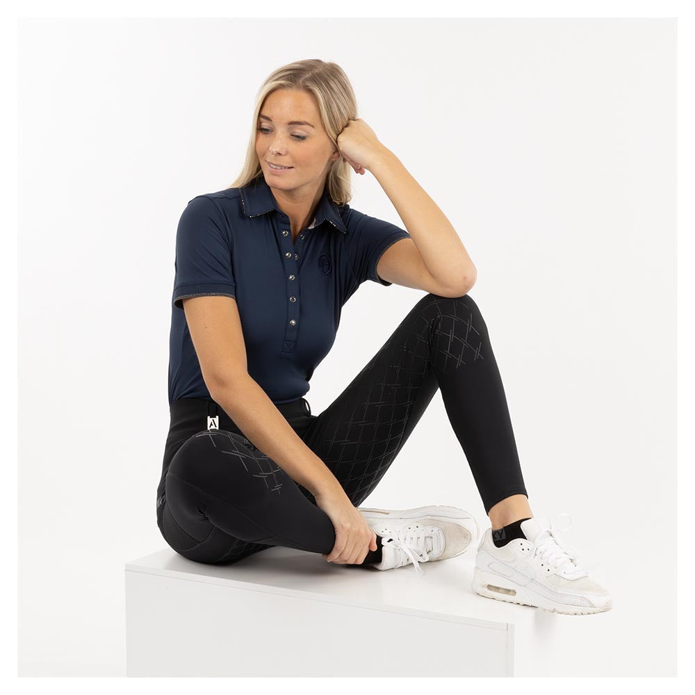 Woman wearing ANKY polo shirt and black breeches, casual pose.