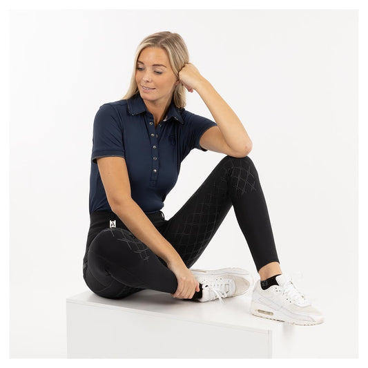 Woman wearing ANKY polo shirt and black breeches, casual pose.