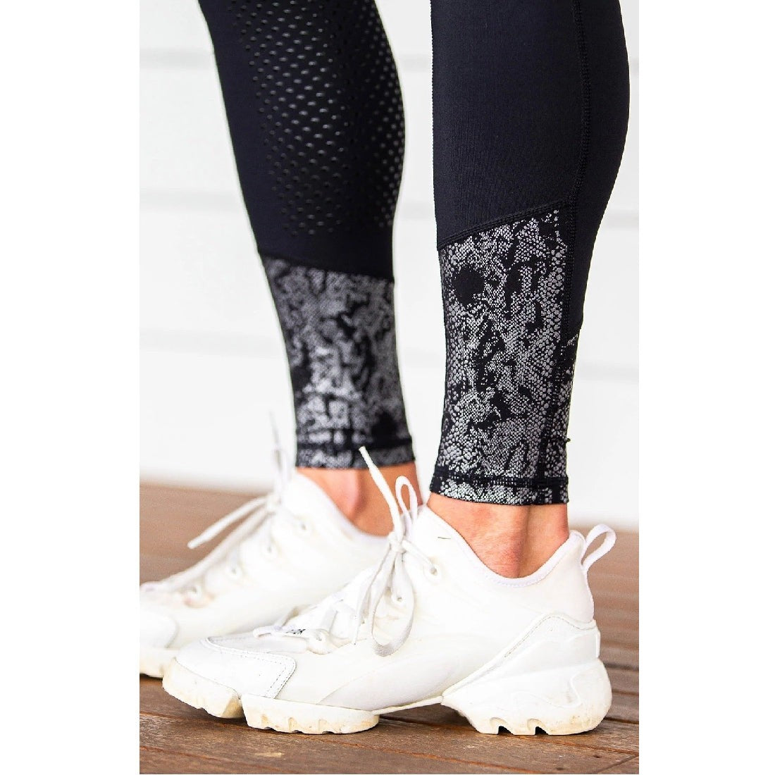 Person wearing black horse riding tights with lace detail and white sneakers.