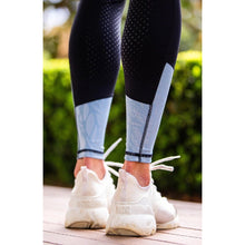 Person standing in horse riding tights and white sneakers outdoors.