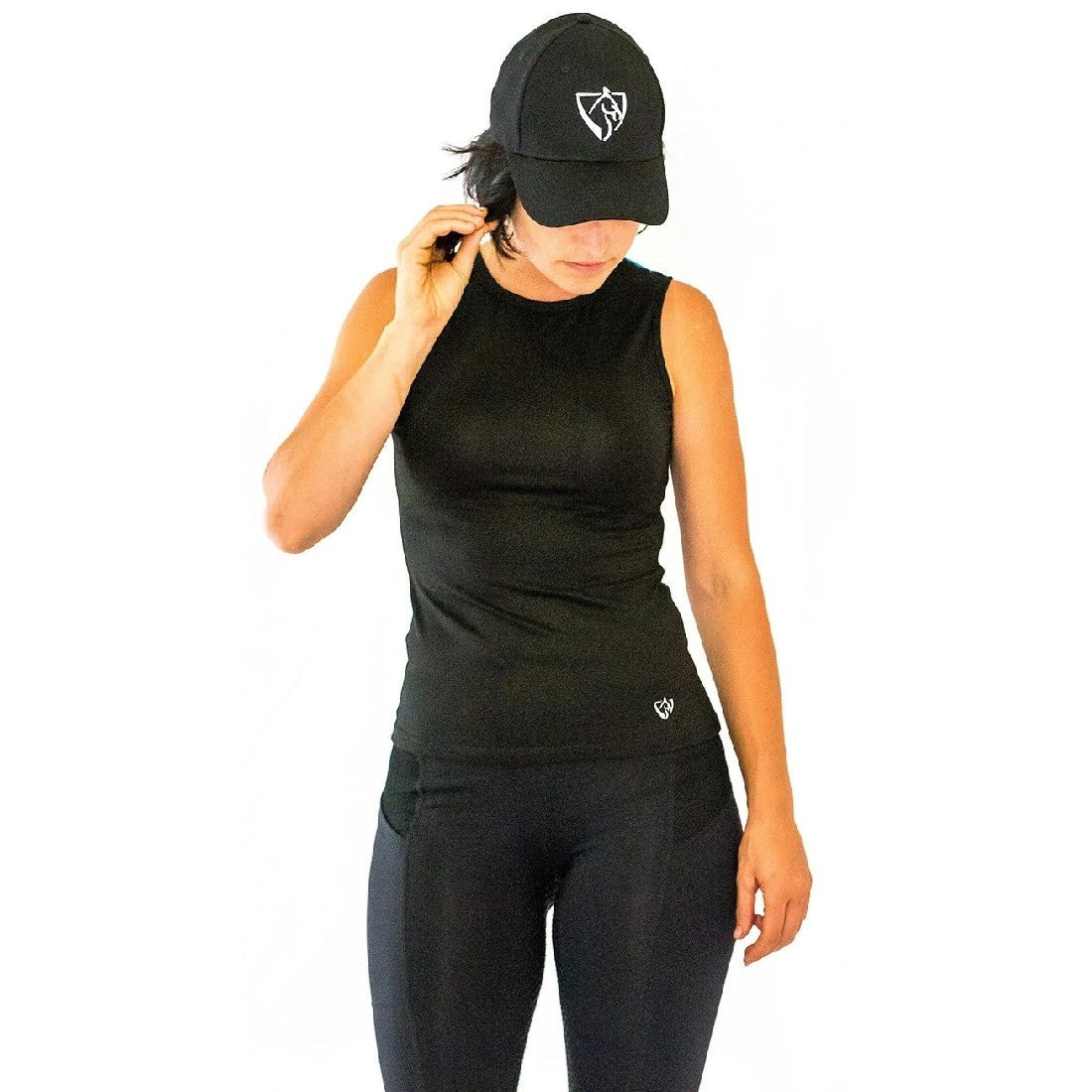 Woman in black cap and horse riding tights standing against white background.