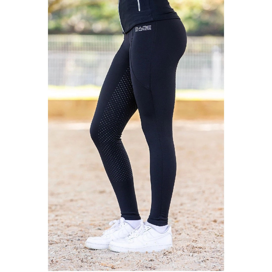 Person in black horse riding tights with dot detailing standing.
