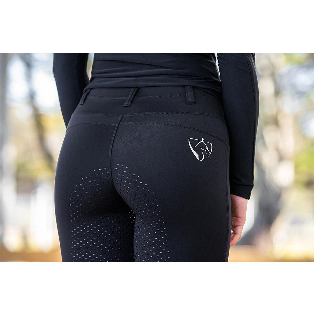 Person wearing black horse riding tights with a logo outdoors.