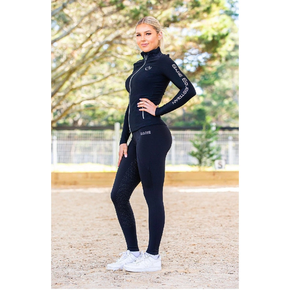 Woman posing in black horse riding tights and matching long-sleeve top.