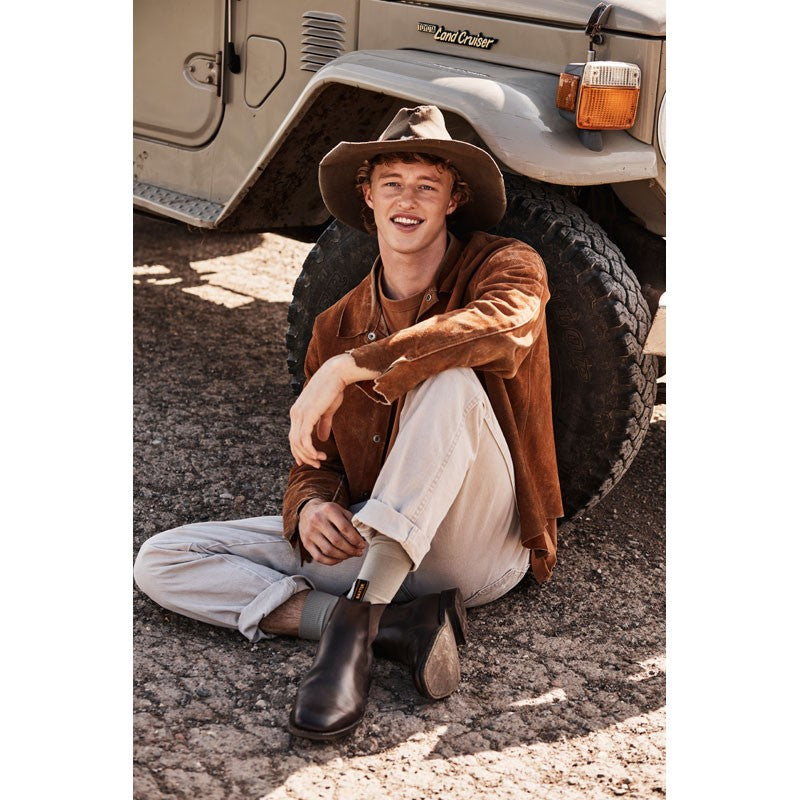 Man in a suede jacket and Baxter Boots sitting by a Land Cruiser.