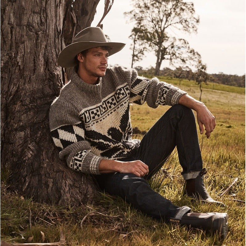 Man in sweater and Baxter Boots leaning against a tree outdoors.