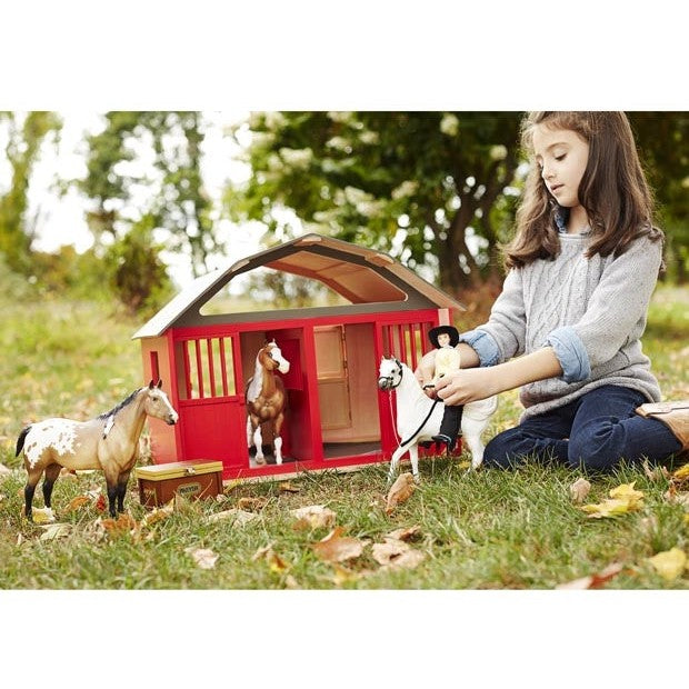 Child plays with Breyer Horse Toys stable and figurines outdoors.
