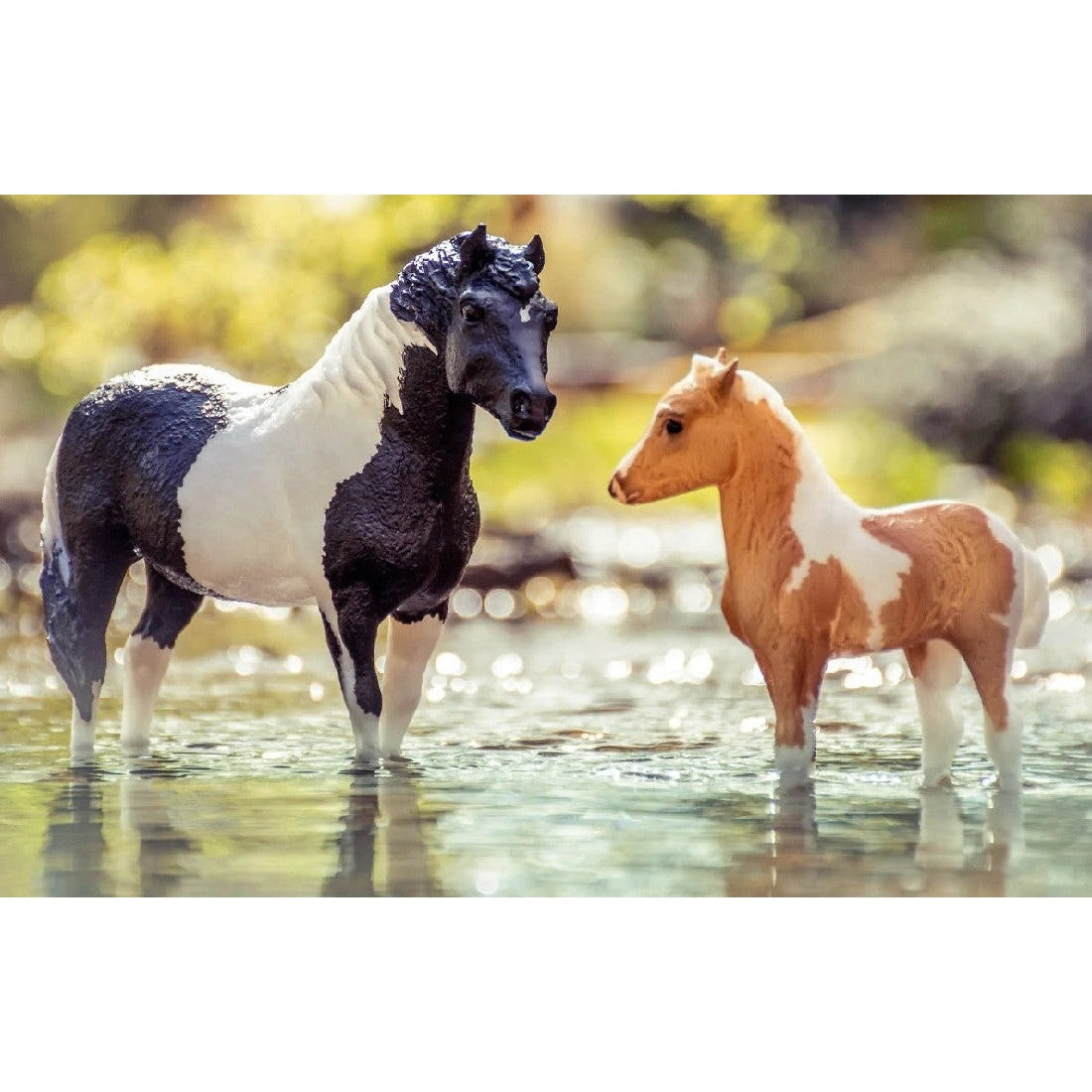Two Breyer Horse Toys standing in shallow water, one black and white.