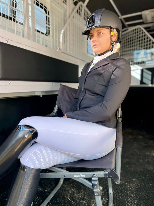 Rider in equestrian helmet and horse riding tights seated thoughtfully.