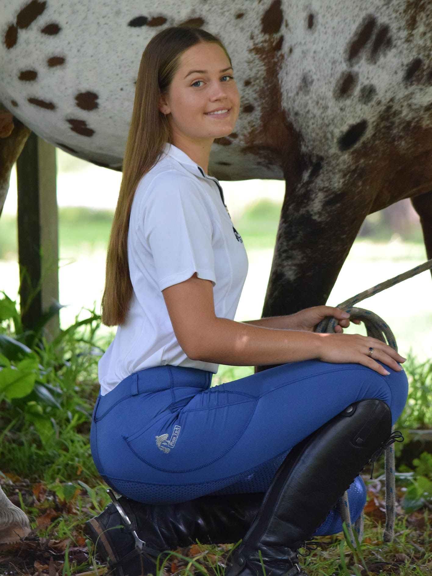 Woman sitting by horse in blue horse riding tights and boots.