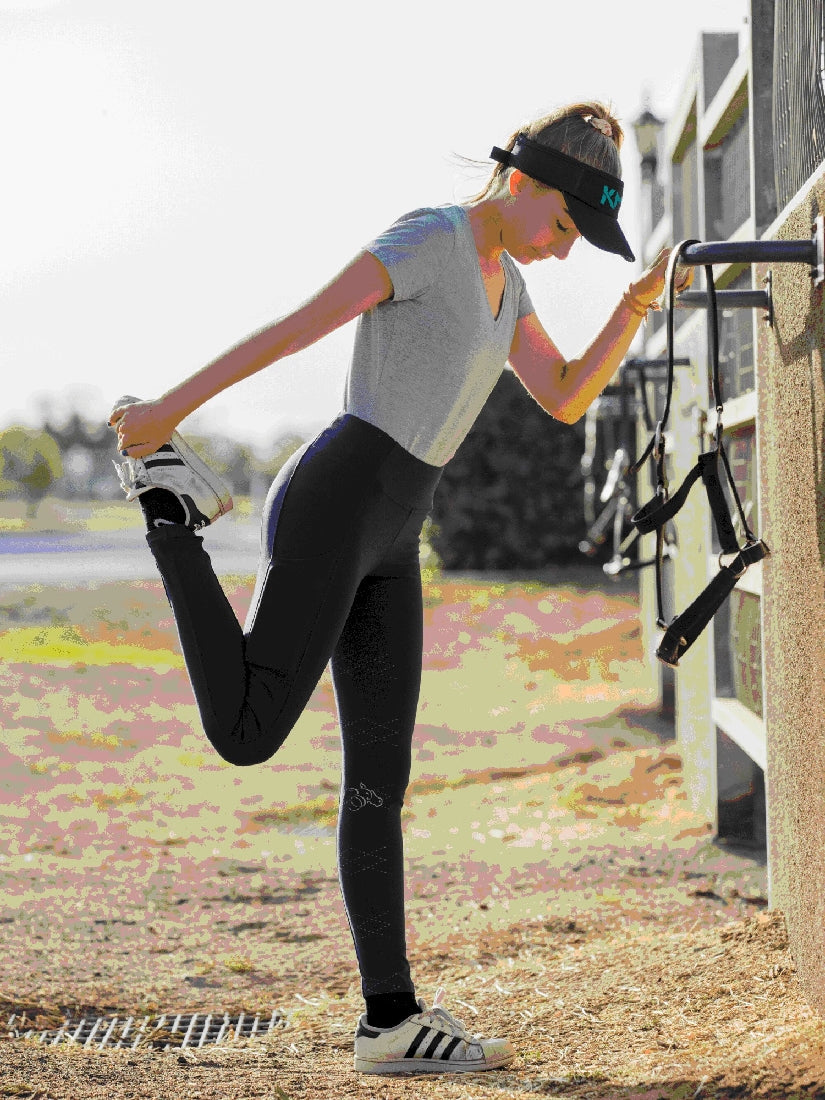 Woman stretching leg wearing horse riding tights and sports visor.