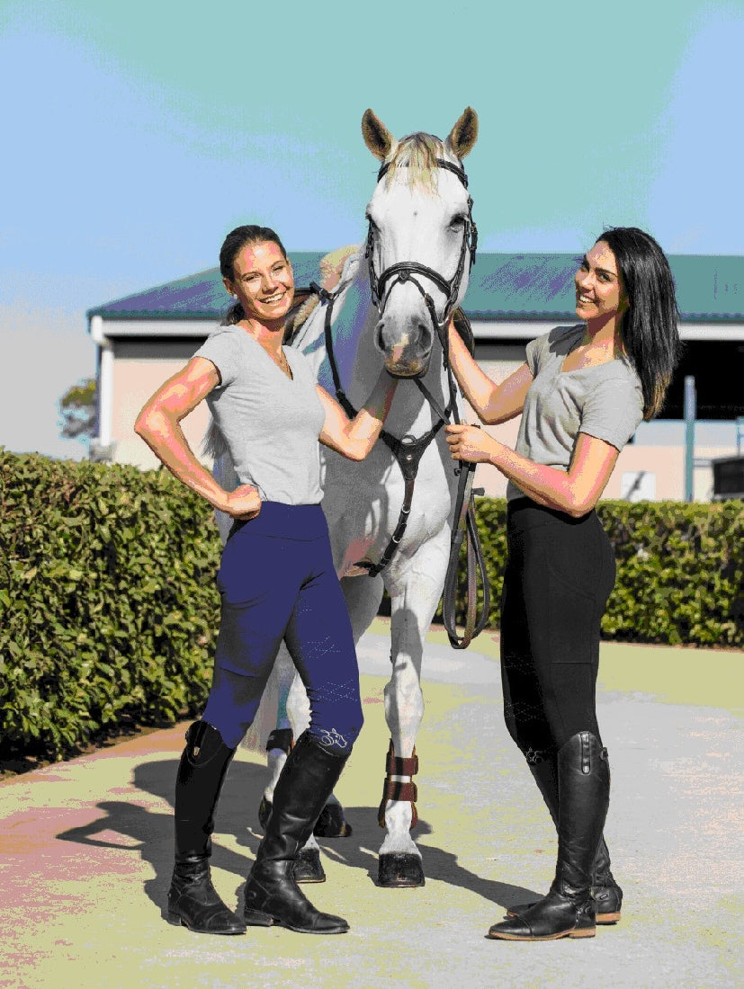 Two smiling women in horse riding tights standing with a white horse.