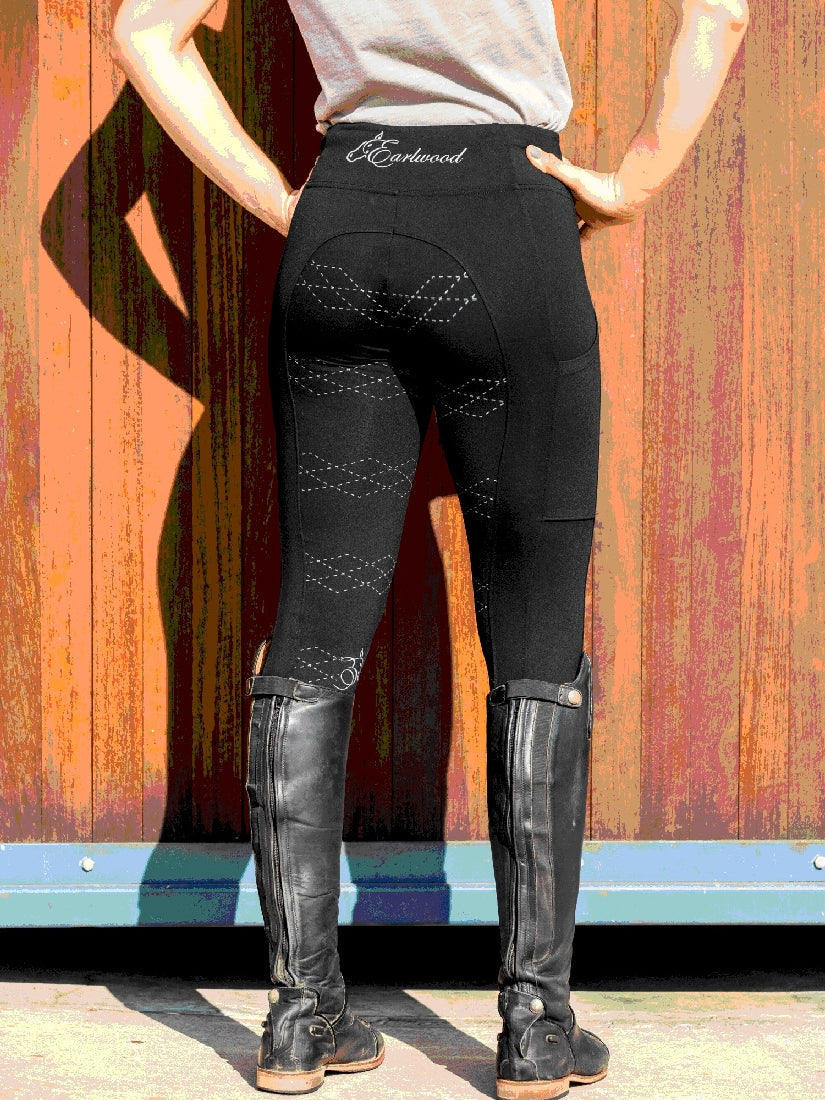 Person in black horse riding tights and boots facing away.