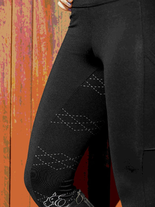 Close-up of black horse riding tights against a rusty background.