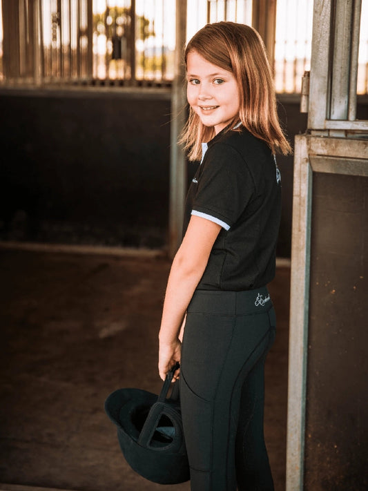 Young girl in stable wearing black horse riding tights, holding helmet.