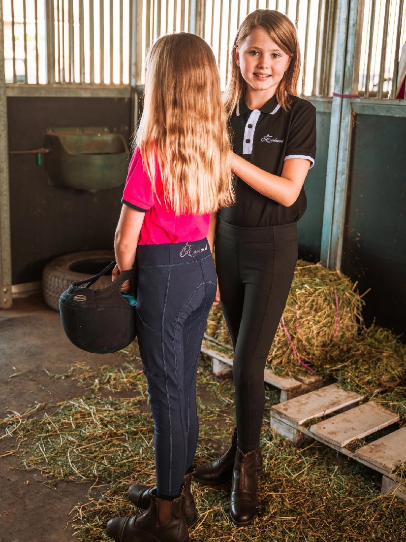 Two girls in horse riding tights standing in a stable.