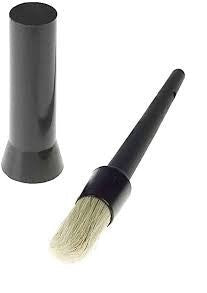 A lens cleaning brush with a black handle laying next to its cylindrical storage container on a white background.