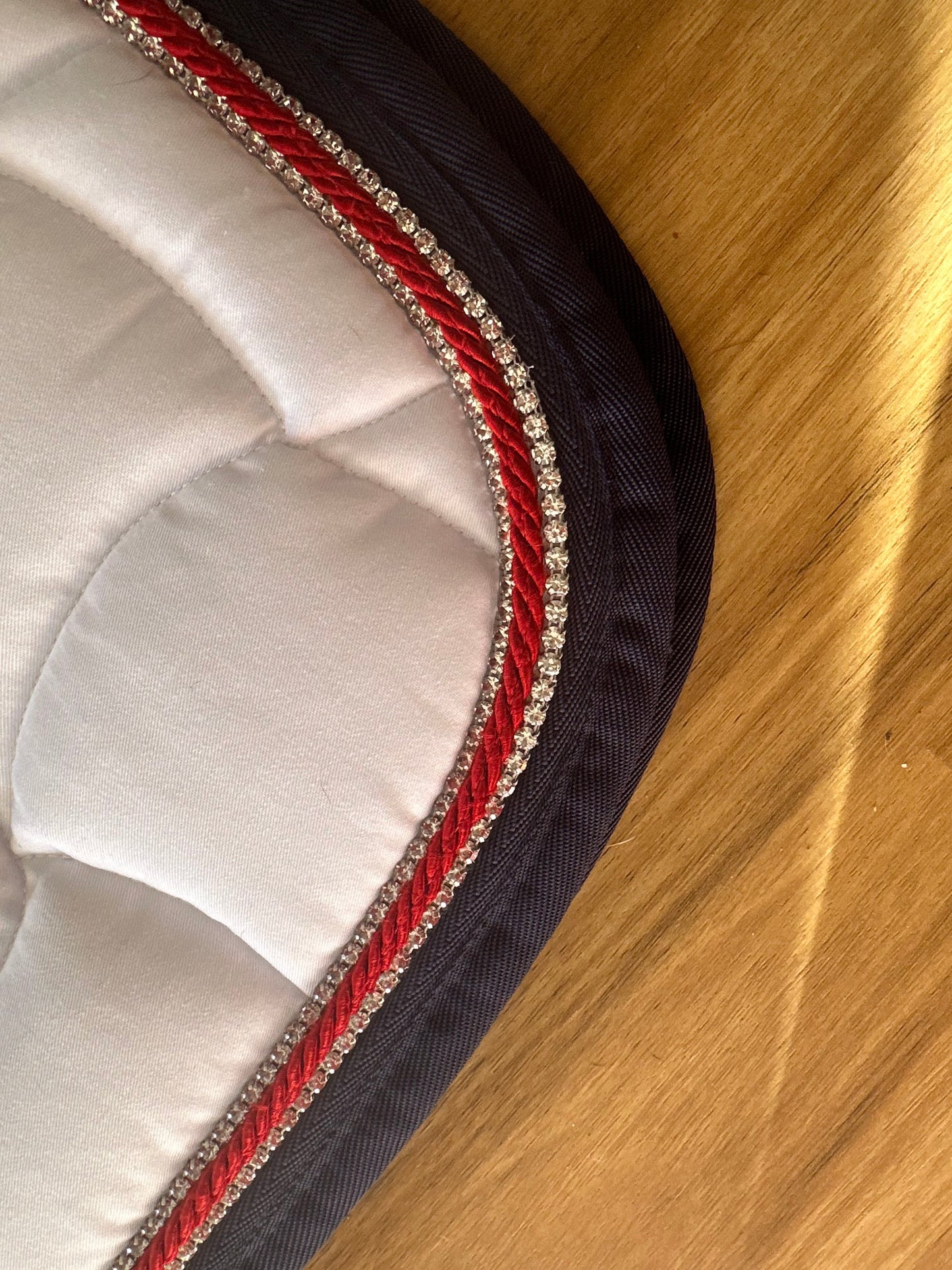 Alt text: Close-up Anna Scarpati saddle pad with red and crystal trim.