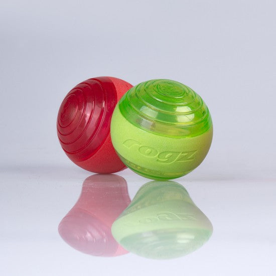 Two Rogz dog balls, red and green, on reflective surface.