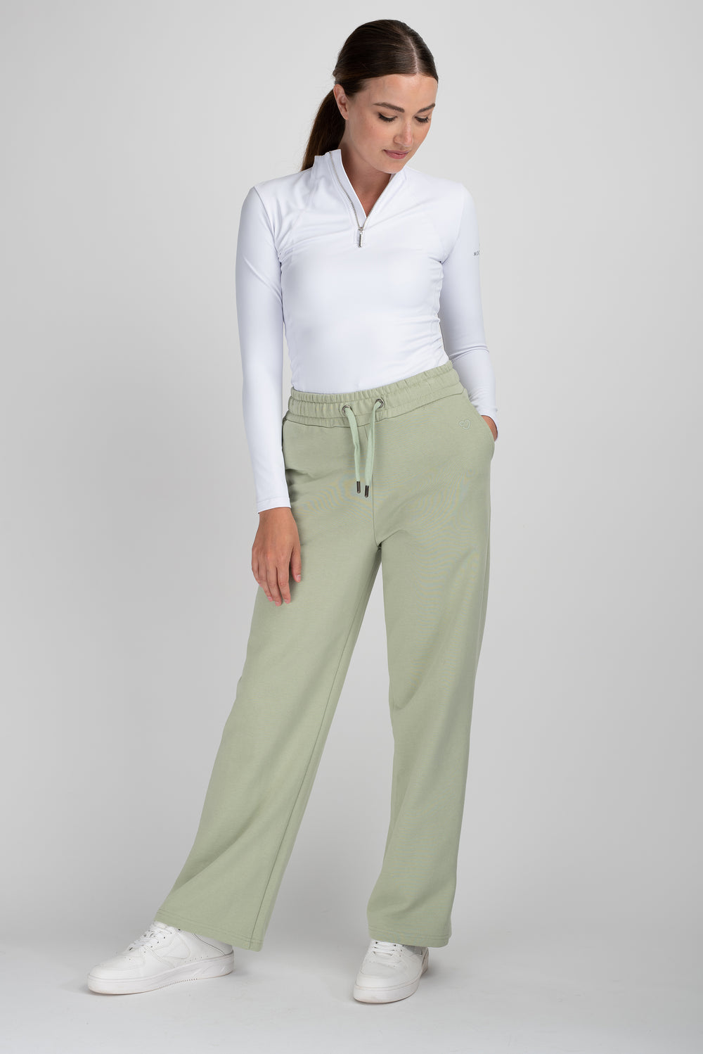 Woman in white top and green horse riding tights standing.
