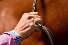 Close-up of hand gripping Thinline horse reins, vibrant background.