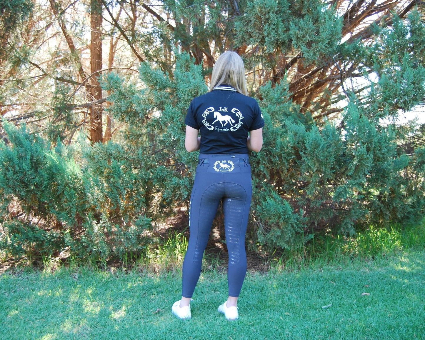 Woman standing in garden wearing horse riding tights and black shirt.