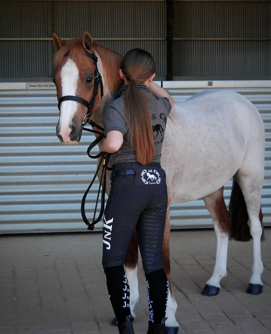 Person in horse riding tights embraces a brown and white horse.