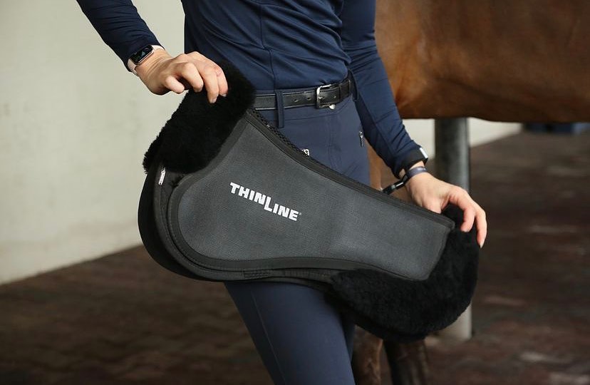 Person holding Thinline black saddle pad beside a brown horse.
