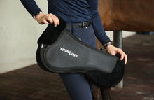 Person holding Thinline black saddle pad beside a brown horse.