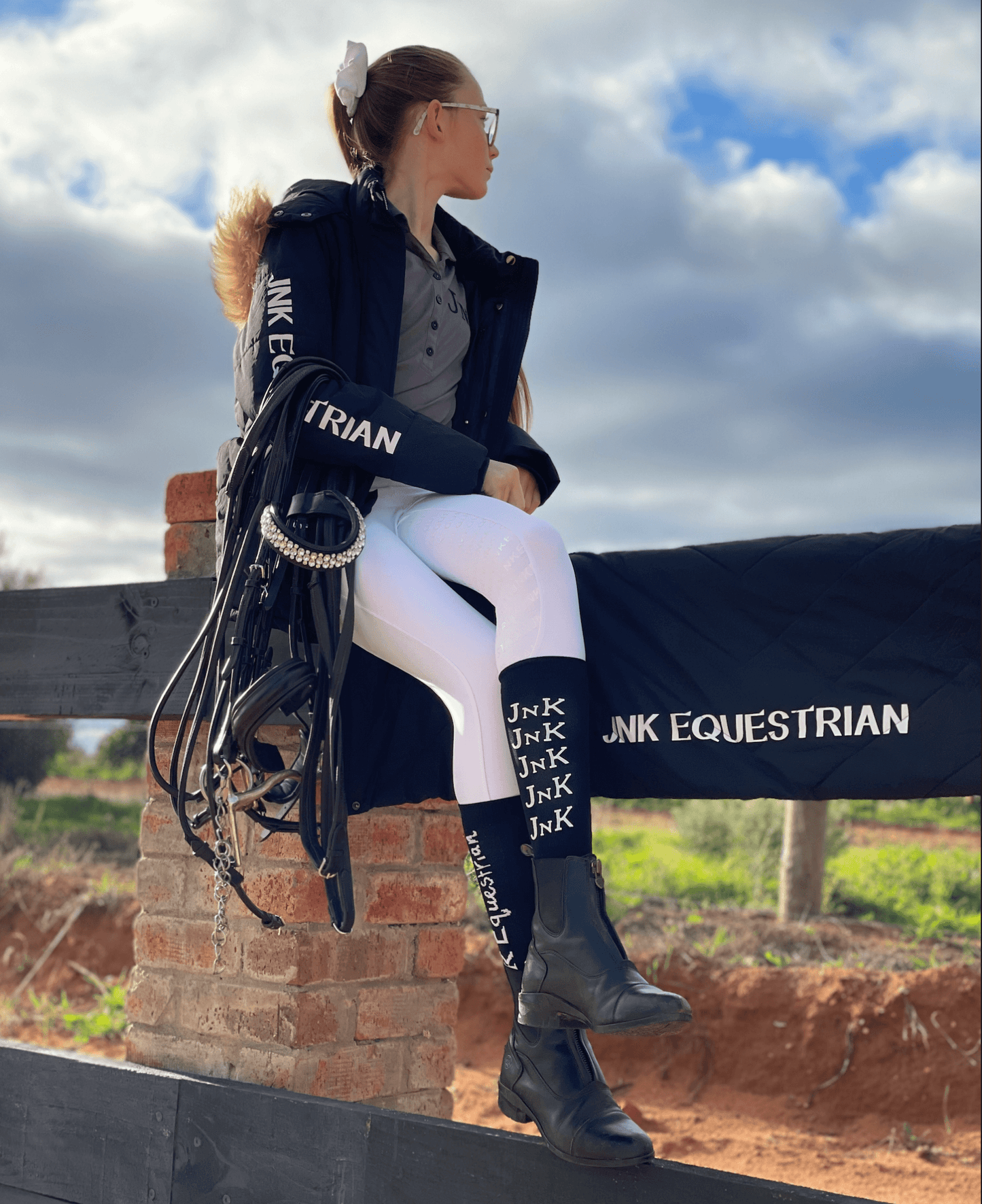 Woman in equestrian attire with horse riding tights sitting outdoors.